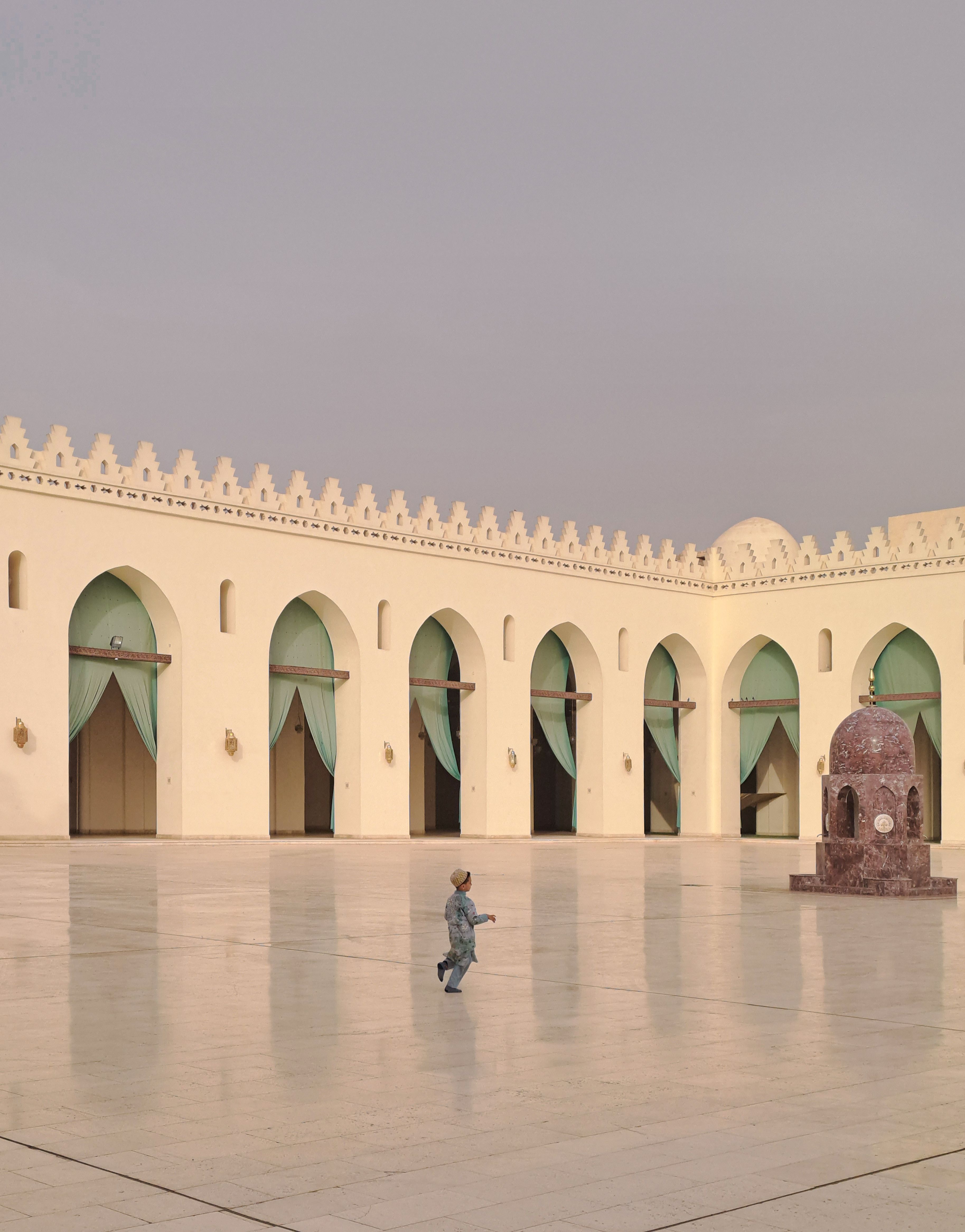 A boy runs through the courtyard of Al-Hakim Mosque in Cairo, Egypt, showcasing its architectural beauty.
