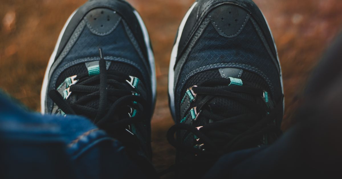 A close-up view of trendy black sneakers worn outdoors, resting on a natural surface.