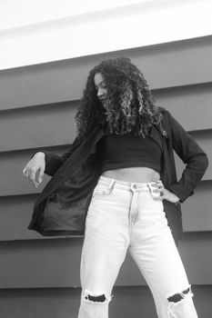 Black and white photo of a fashionable woman posing against a modern wall, showcasing style and attitude.