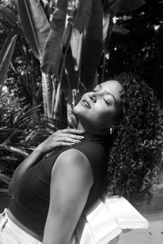 Black and white portrait of a woman with curly hair outdoors, enjoying the sun.