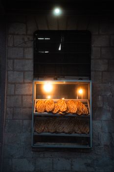 Loaves of bread showcased in a bakery window, warmly lit against brick walls at night.