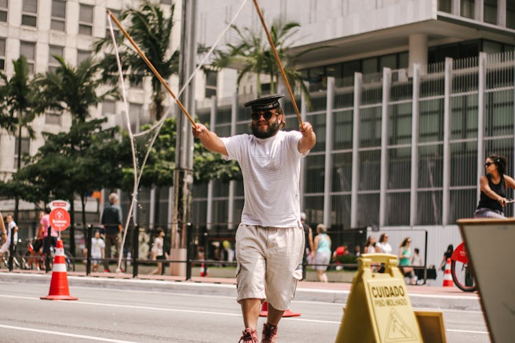 Man In White T-shirt And Beige Shorts Holding Two Sticks