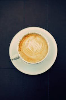 Top view of a cappuccino with intricate latte art in a white cup on a dark background.