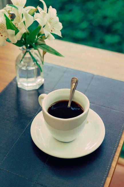 A classy coffee cup and saucer on a table with a vase of white flowers, perfect for a cozy café setting.