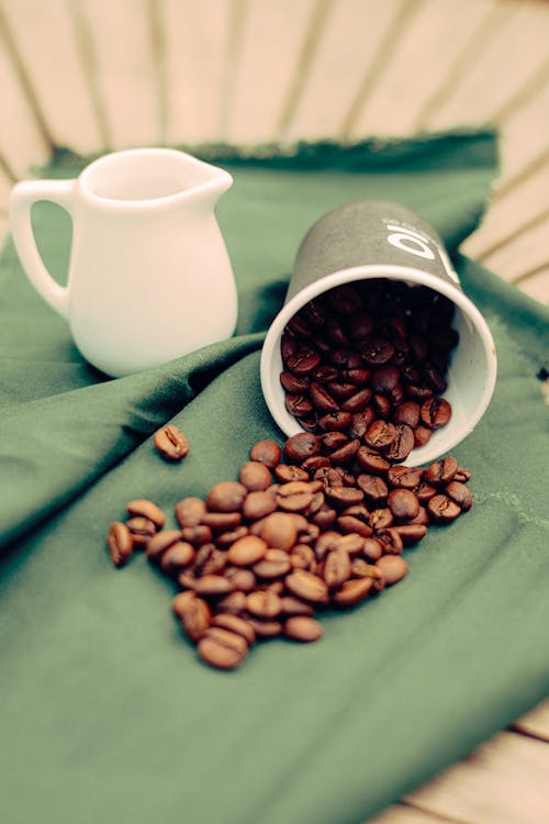 Coffee beans and a pitcher sit on a green cloth