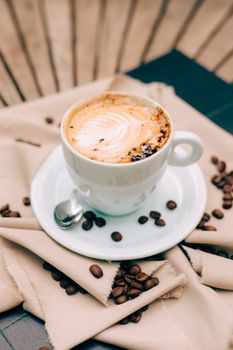 Elegant cup of cappuccino with froth art surrounded by coffee beans on a napkin.