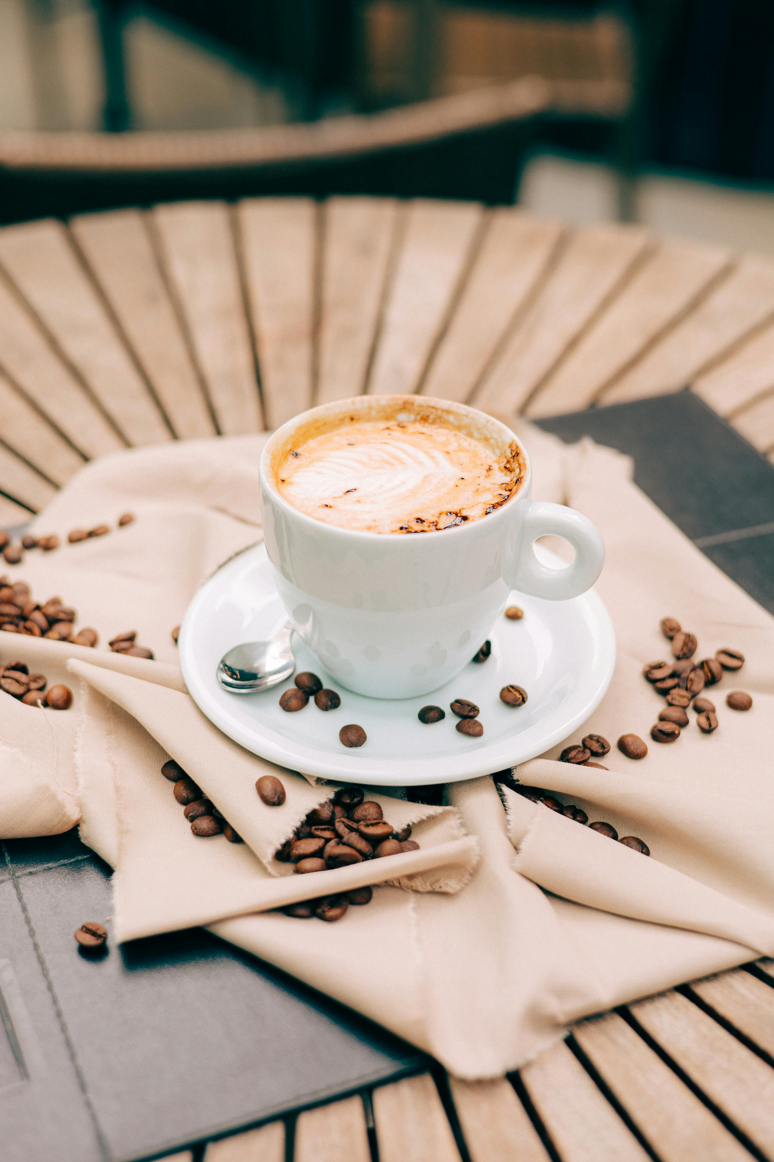 A beautifully crafted cappuccino surrounded by coffee beans on a rustic wooden table.