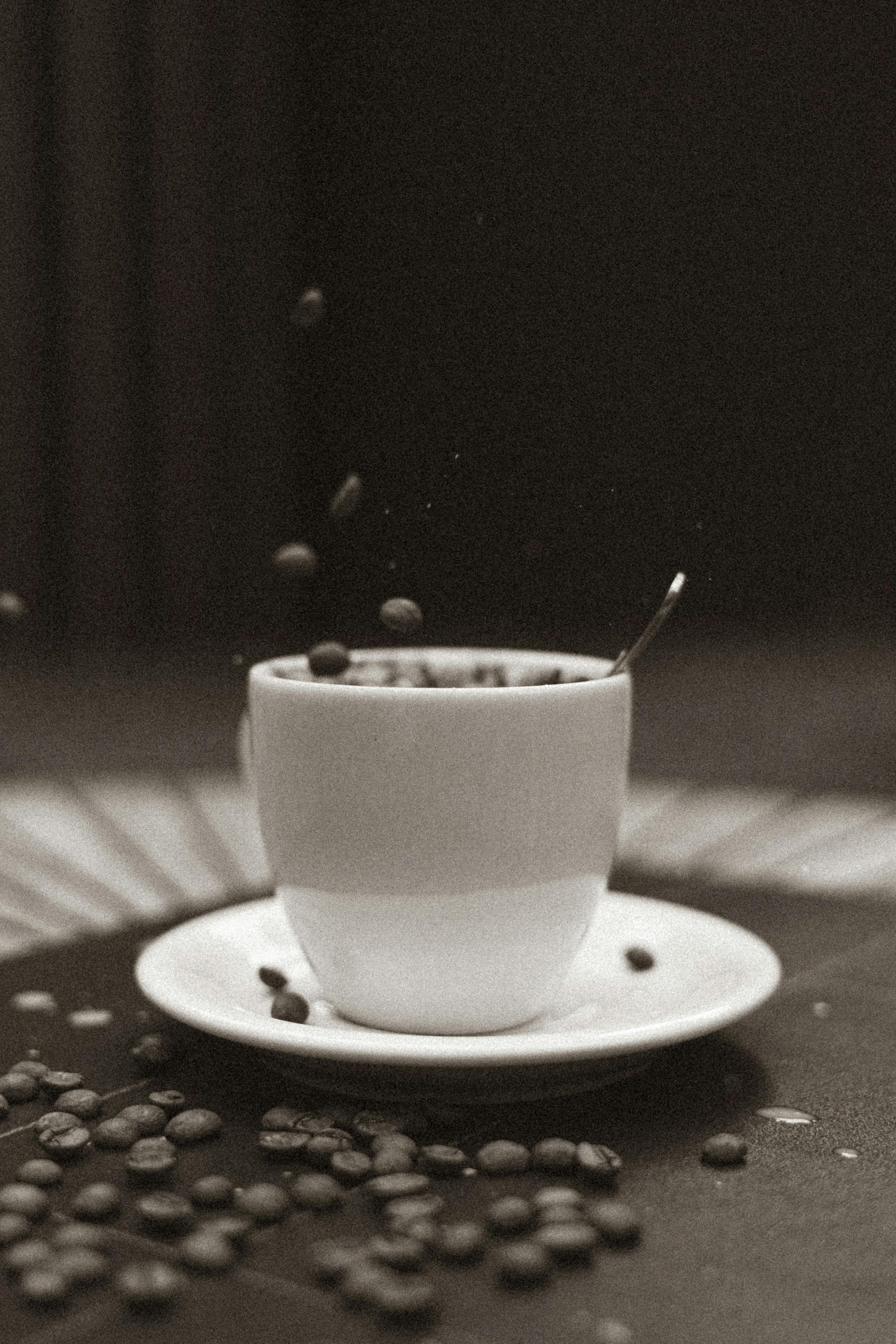 A vintage black and white photo of coffee beans spilling into a cup, creating a dynamic still life.
