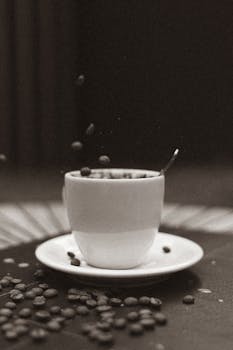 A vintage black and white photo of coffee beans spilling into a cup, creating a dynamic still life.