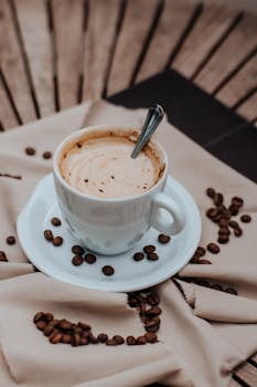 Close-up of a cappuccino with foam, surrounded by scattered coffee beans and a spoon.
