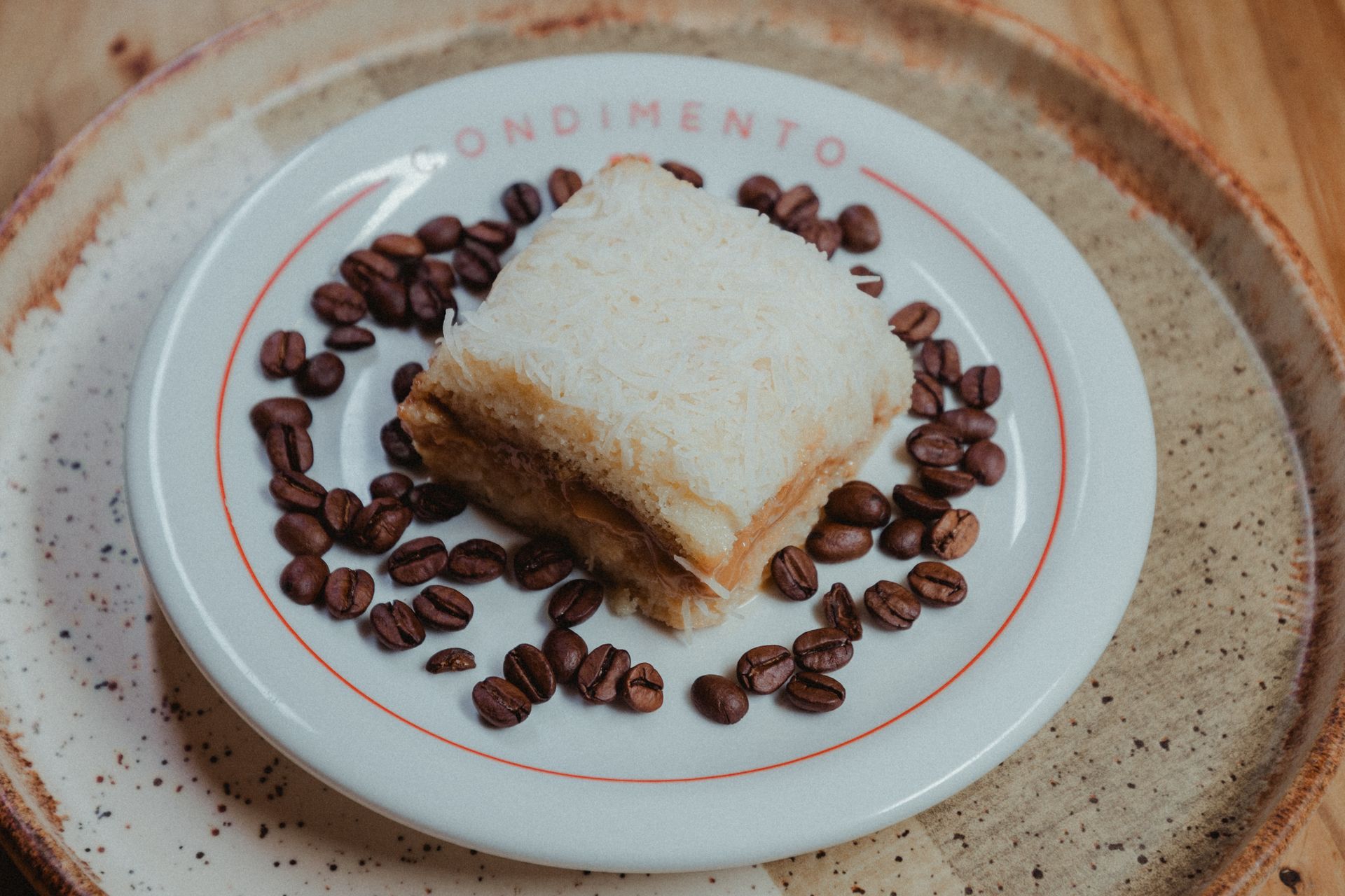 A slice of creamy coconut cake garnished with coffee beans on a rustic plate.