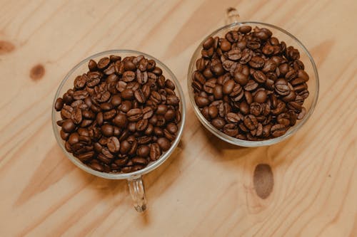 Two cups of coffee beans on a wooden table