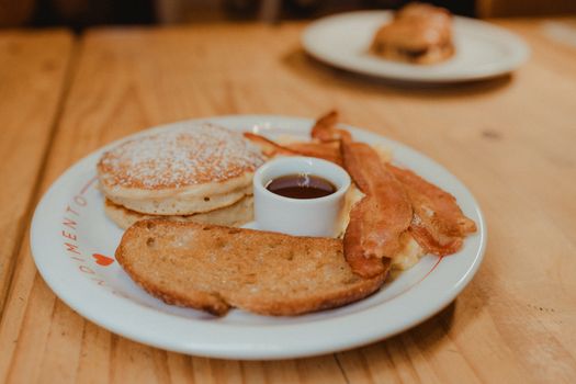 Enjoy a delightful breakfast with pancakes, bacon, toast, and syrup on a wooden table.