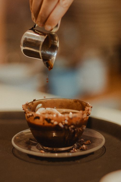 Free Close-up of hand pouring chocolate syrup onto a dessert bowl on a tray. Stock Photo