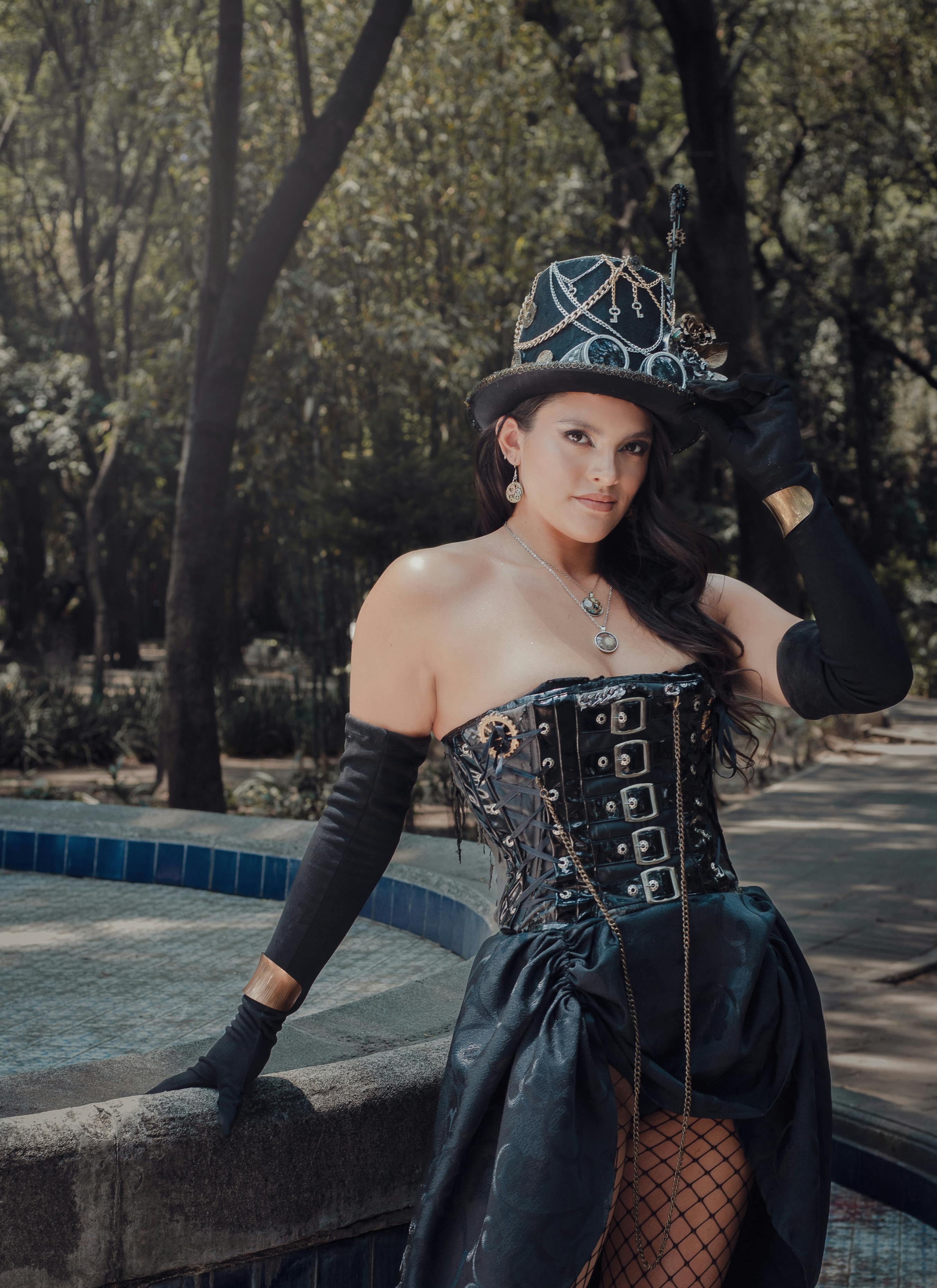 A stylish steampunk fashion portrait of a woman in an urban park, showcasing a corset and elaborate hat.
