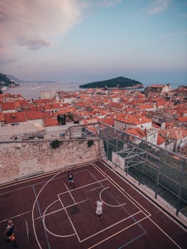 Basketball court with players in a coastal Croatian town with red rooftops and sea view.