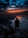 一名男子在希腊悬崖上的剪影，欣赏着海洋上充满活力的日落