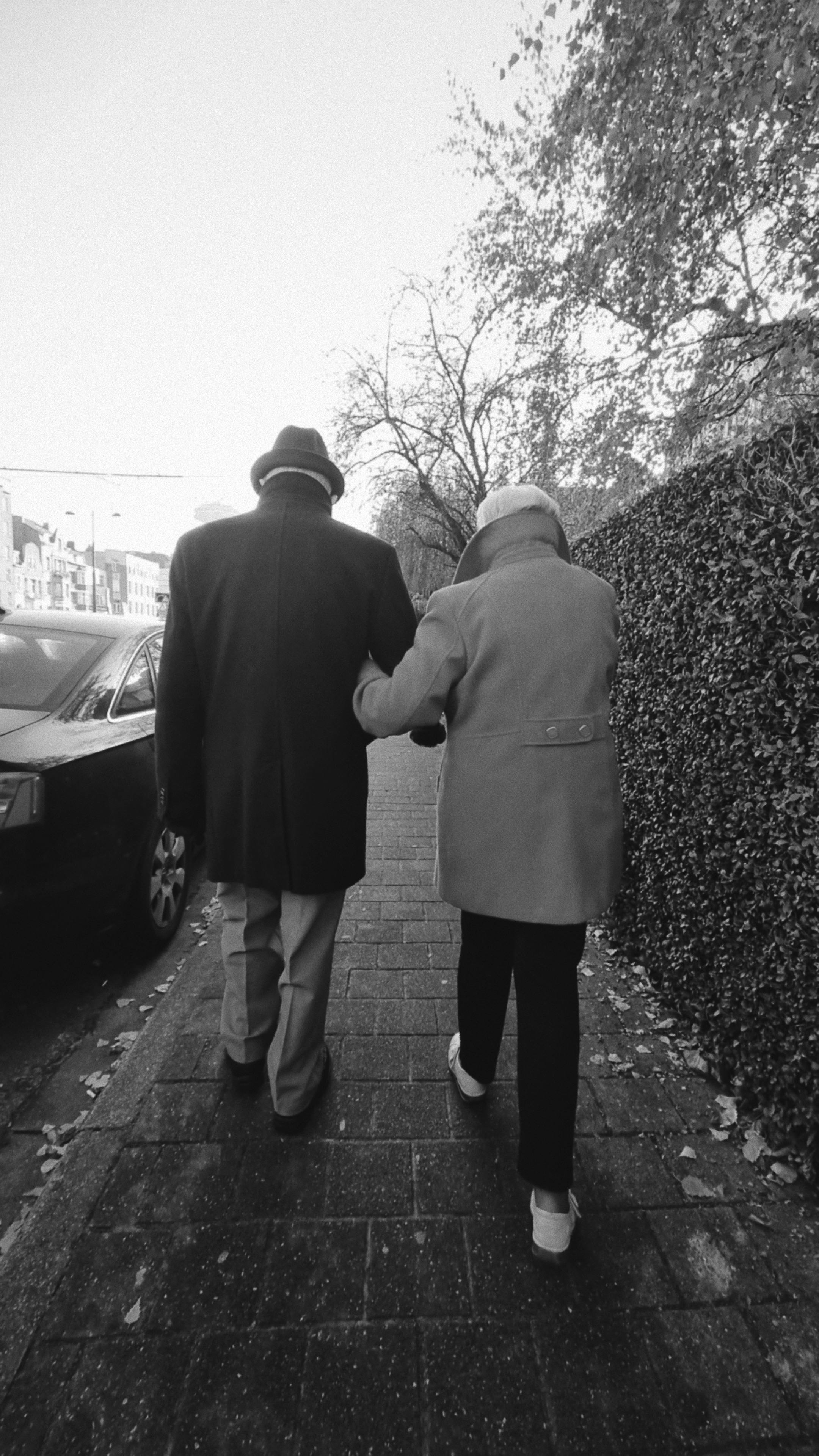 A senior couple walking arm in arm down a city sidewalk, enjoying a peaceful autumn day.