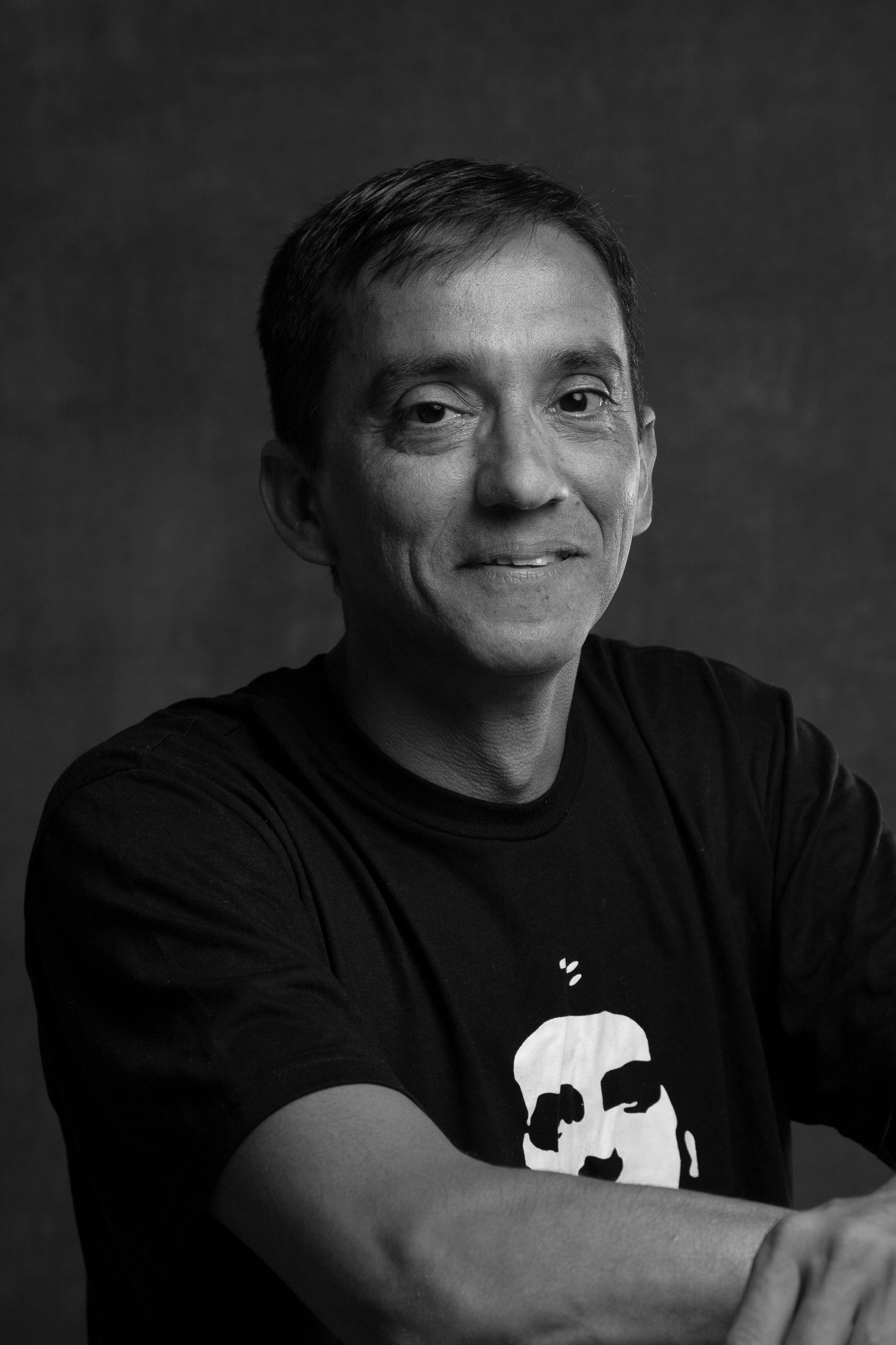 Studio portrait of a smiling man in a black t-shirt, capturing a candid and friendly expression.