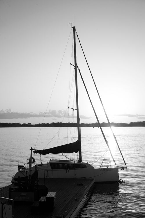 Free A sailboat moored at a pier at sunset, reflecting on calm waters in black and white. Stock Photo