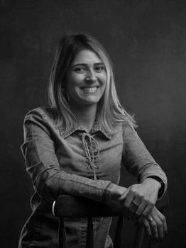 Monochromatic studio portrait of a smiling woman leaning on a chair.