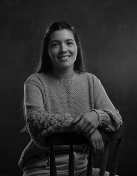 Black and white portrait of a young woman smiling while seated in a studio setting.