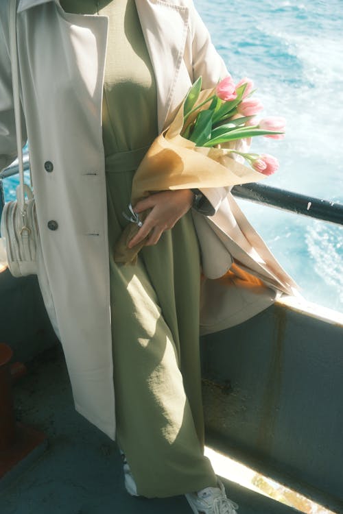 A woman in a green coat holding flowers on a boat