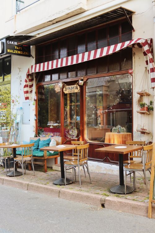Free A cozy outdoor café with striped awnings, wooden chairs, and tables on the sidewalk. Stock Photo