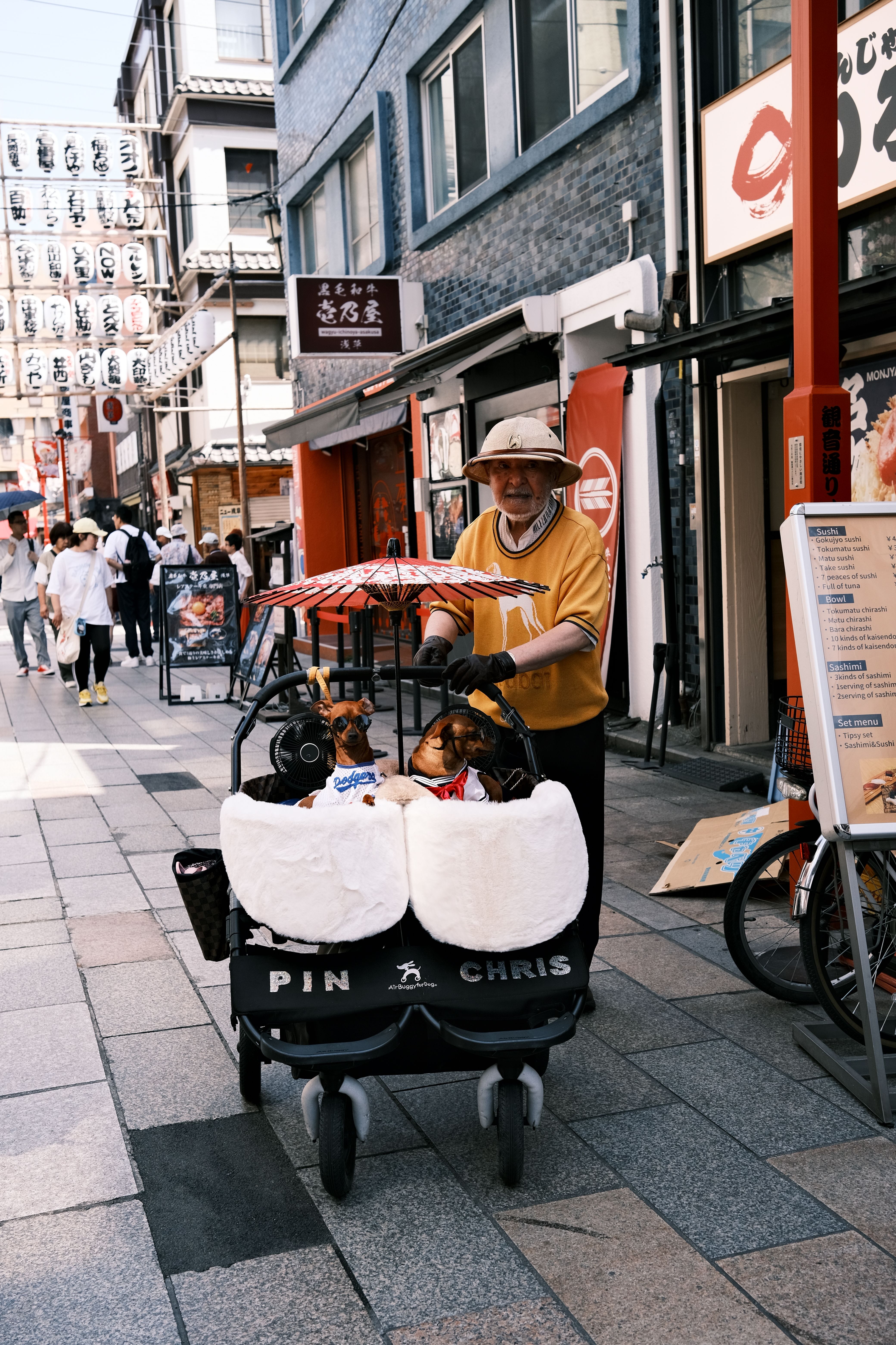 Elderly man walking dogs in stroller on bustling Tokyo street, showcasing urban lifestyle.
