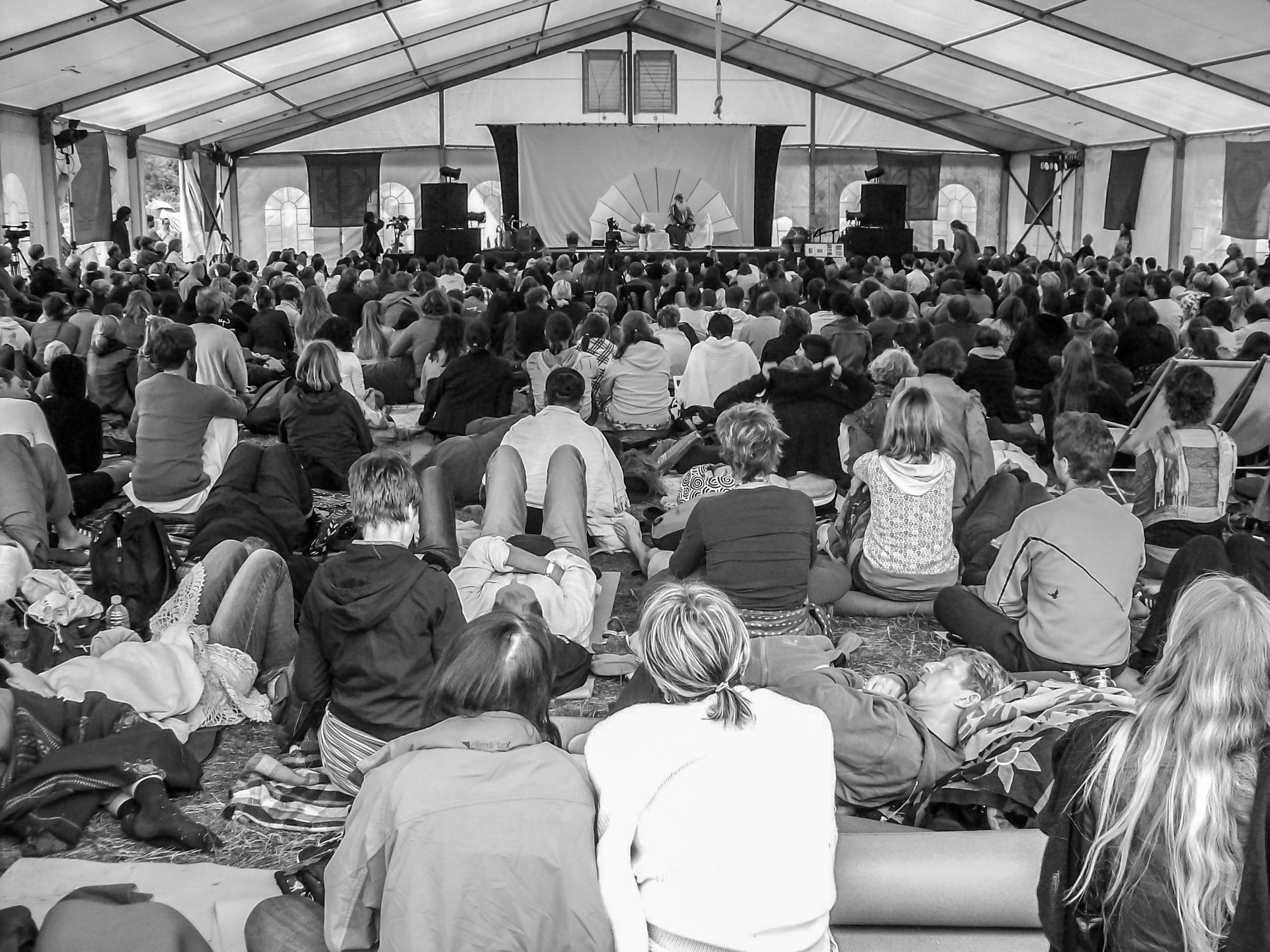 Carpa blanca de un festival de bienestar montada sobre un campo verde, con asistentes sentados en el pasto