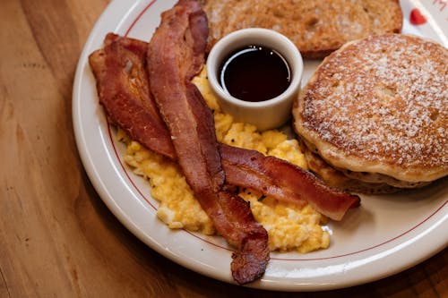 A plate with pancakes, bacon and syrup on it