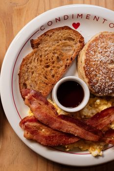 A hearty breakfast featuring pancakes, bacon, scrambled eggs, and toast.