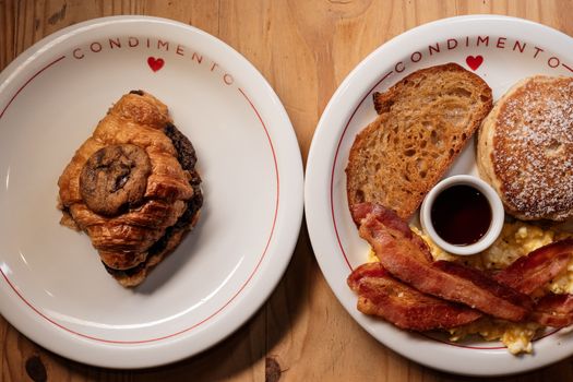 A delectable breakfast spread featuring a croissant and hearty bacon meal on styled plates.