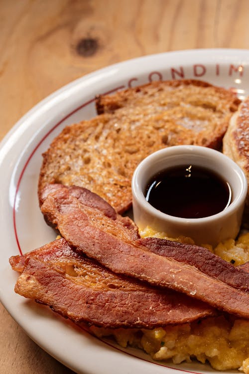 A plate of food with bacon, eggs, toast and syrup