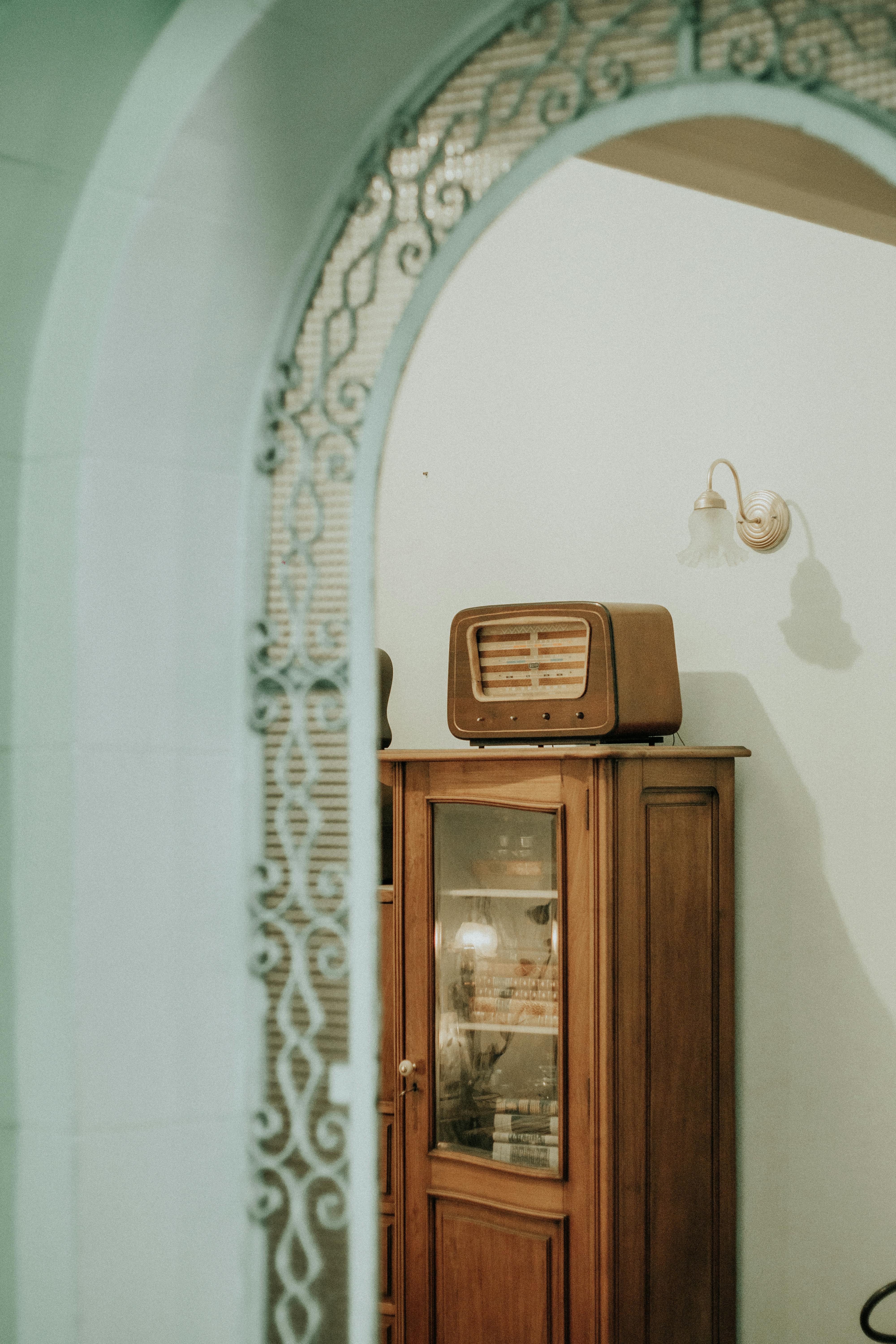 A vintage radio sits atop a wooden cabinet in an elegantly designed room with an ornate archway.
