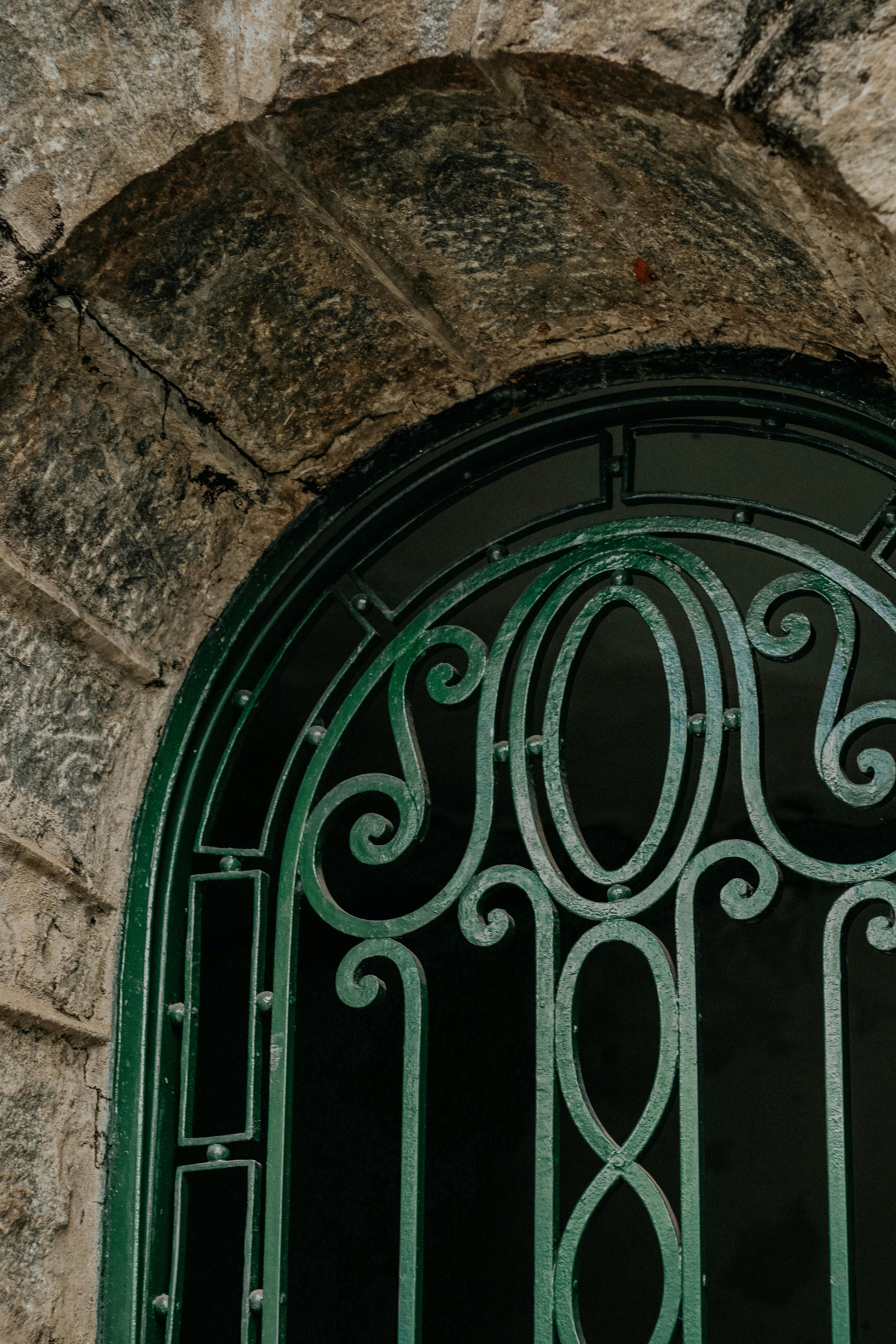 Close-up of green iron lattice window on a historic stone building facade.