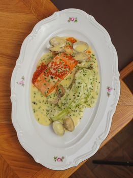 Delicious salmon with rich chive sauce and clams served elegantly on a white platter.