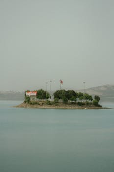 A small island with trees and a Turkish flag in calm blue waters, showcasing tranquility.