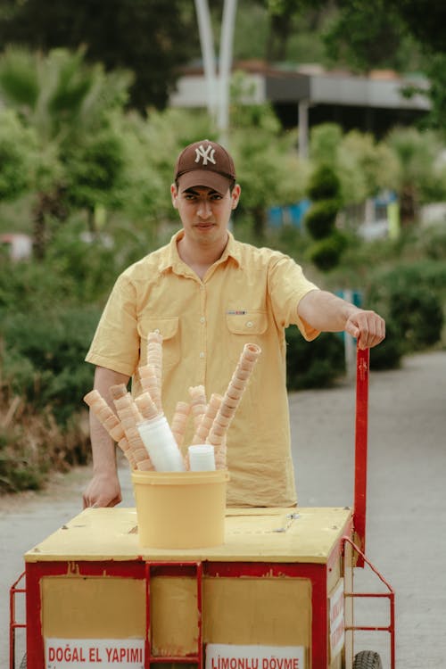 A man in a yellow shirt is holding a cart with ice cream