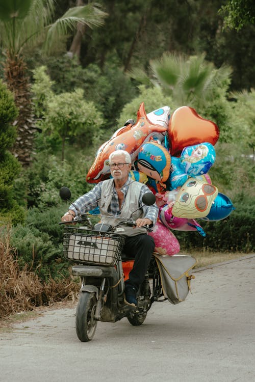 An older man riding a motorcycle with balloons