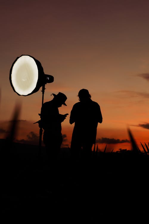 Two people stand in front of a light in the sunset