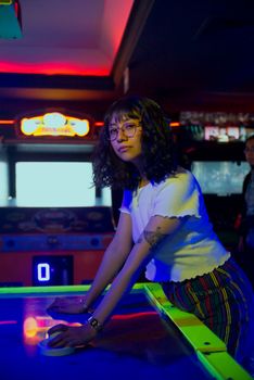 Young woman in an arcade playing air hockey in vibrant lighting, Ciudad de México.