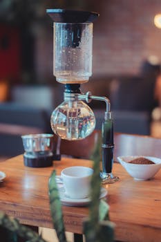 Creative capture of a syphon coffee maker with cup and sugar bowl on a wooden table.