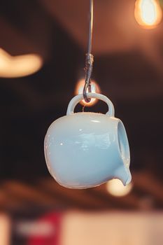 A white ceramic pitcher artistically suspended by a wire indoors.