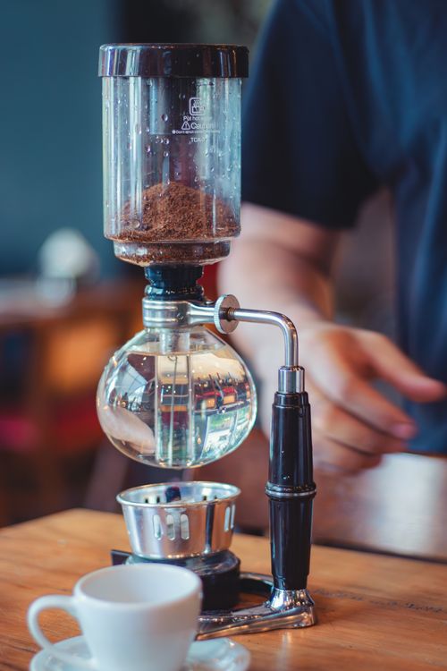 Free Coffee machine preparing fresh brew with focus on hand and cup on wooden table. Stock Photo