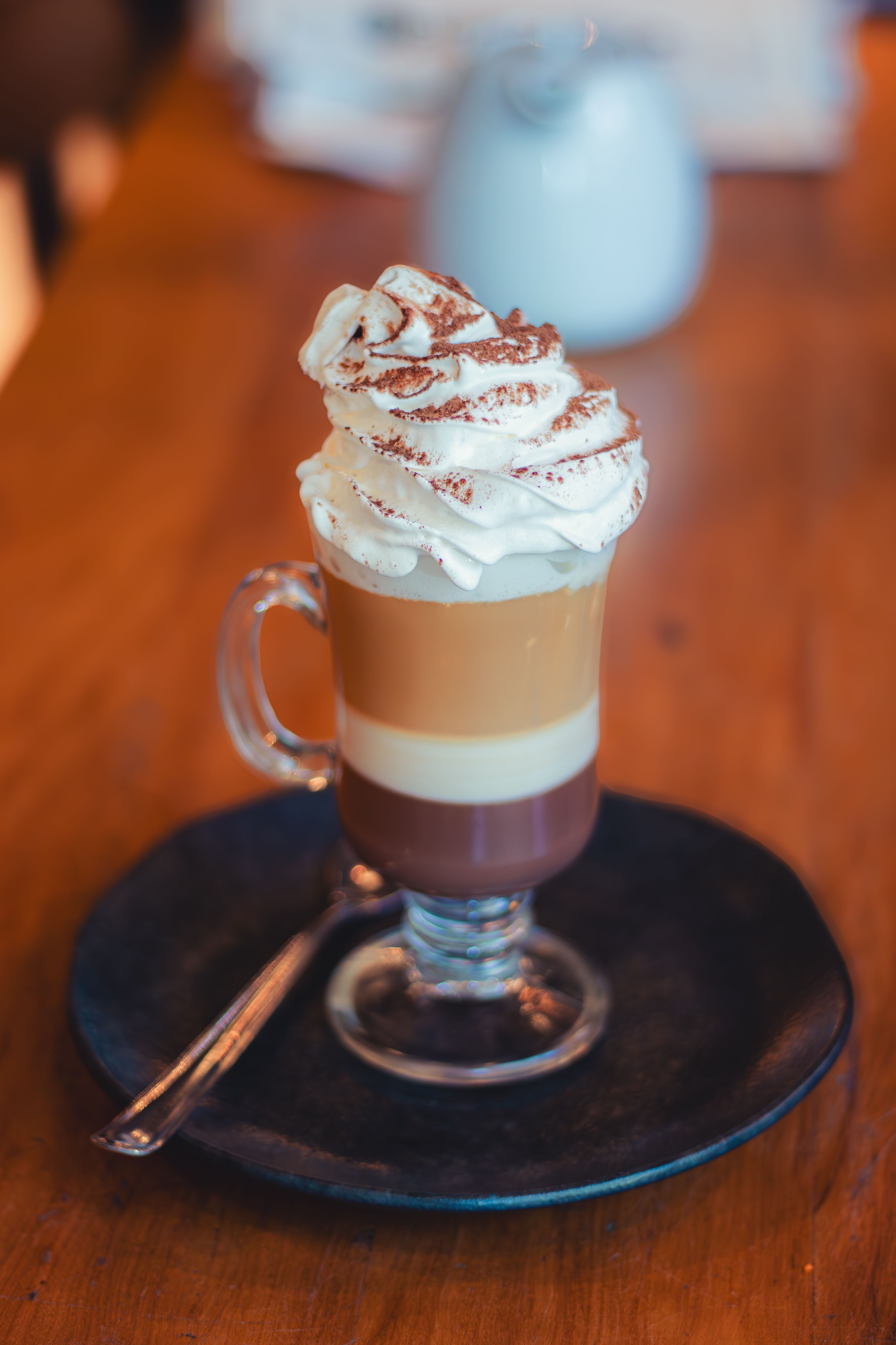 A vanilla latte with light microfoam in a clear glass mug, next to a small pitcher of steamed milk and a espresso shot glass.