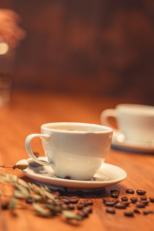 Free A cozy setting with a coffee cup on a rustic wooden table, surrounded by coffee beans. Stock Photo