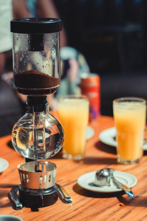 A coffee maker sits on a table with orange juice and orange slices