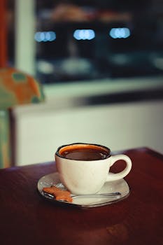 Warm cup of coffee paired with a cookie, placed on a wooden table in a cozy indoor setting.