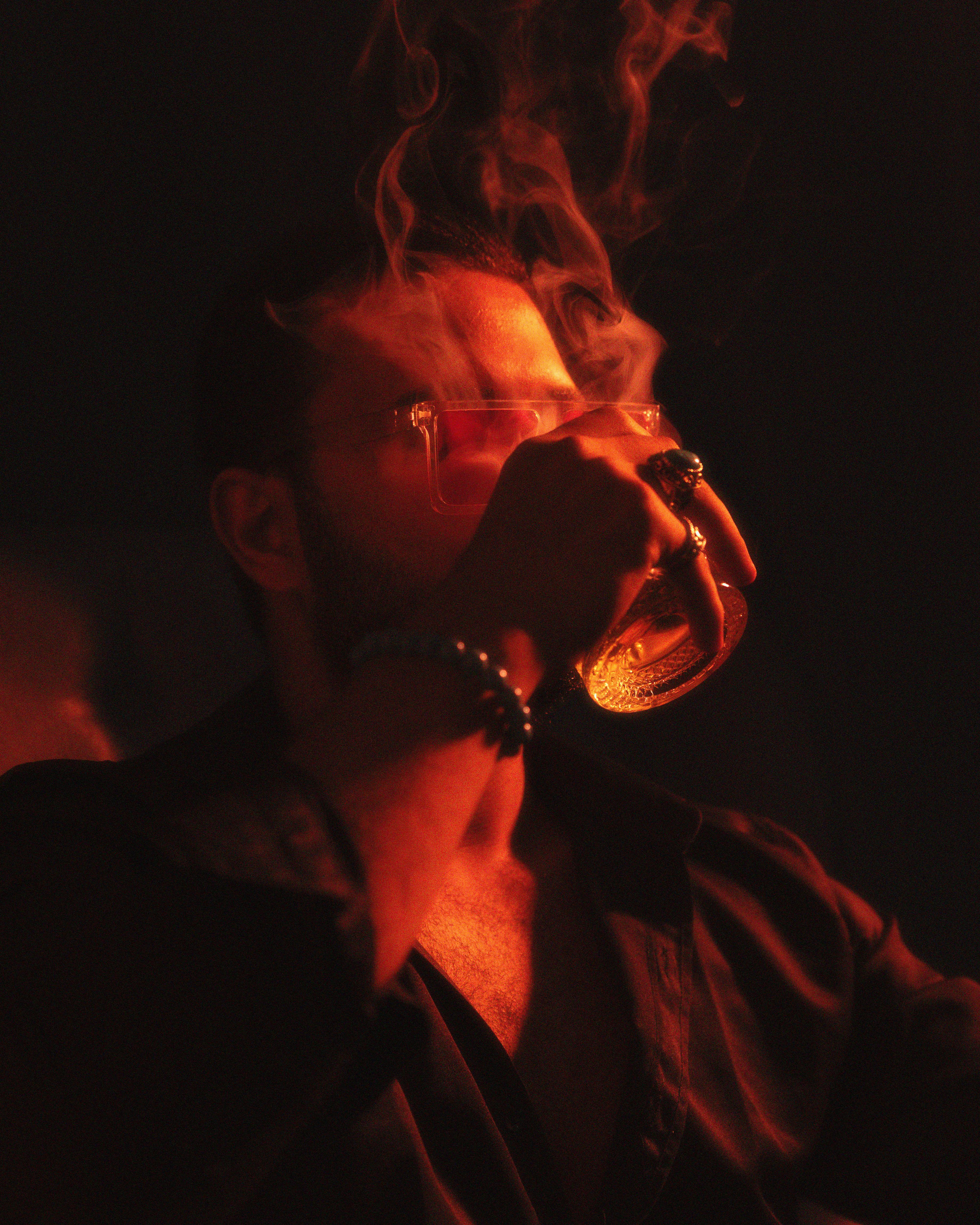 A man drinks from a glass in a smoky, red-lit room, capturing the essence of nightlife.